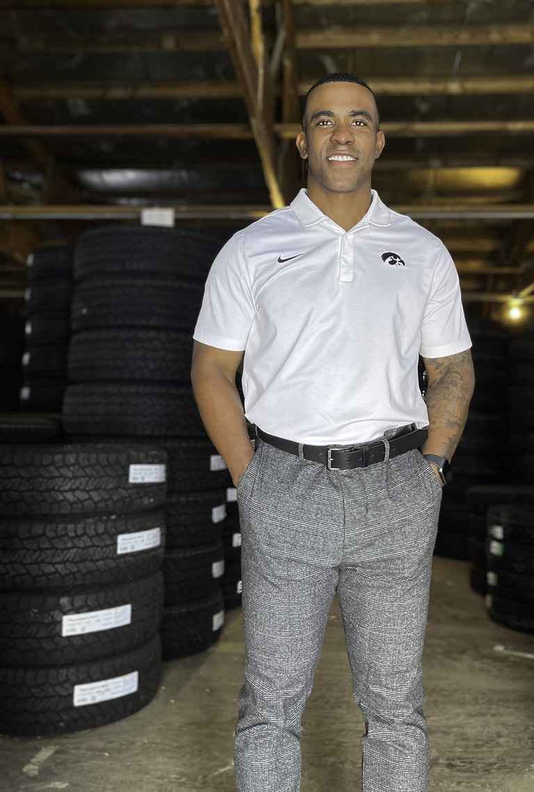 Jason Woodson stands in a Hawkeye polo shirt in front of stacks of tires.