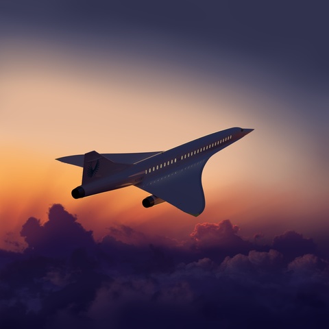 Boom Supersonic aircraft banking with sunset in the background.