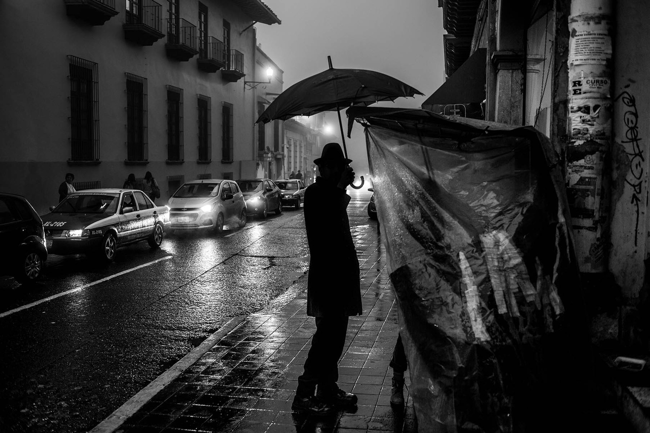 Man holding an umbrella in a Latin American city.