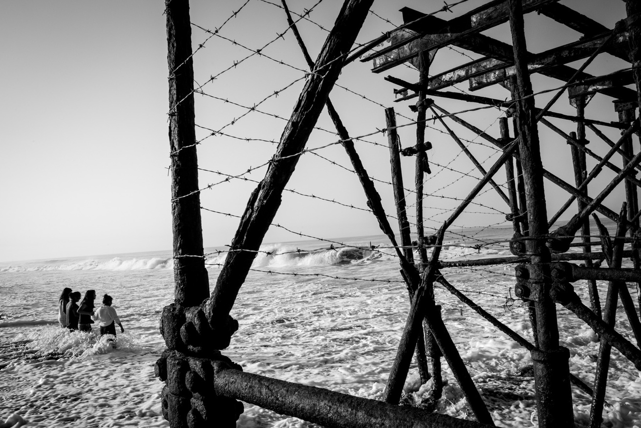 People wading in the ocean in Guatemala with razorwire on a metal structure in the foreground.