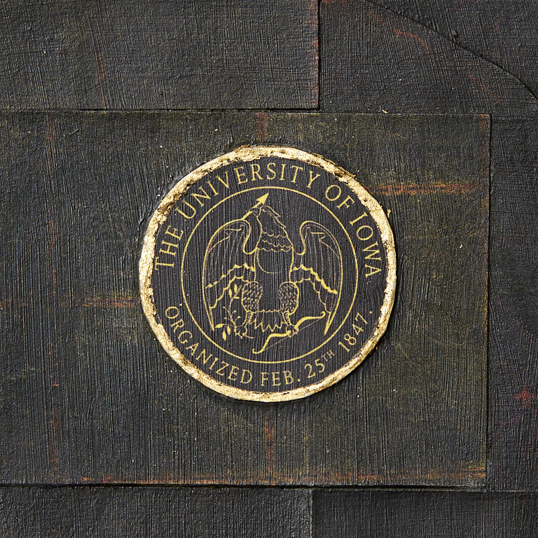 The University of Iowa official seal as a lapel pin, circled in golden metal leaf. 