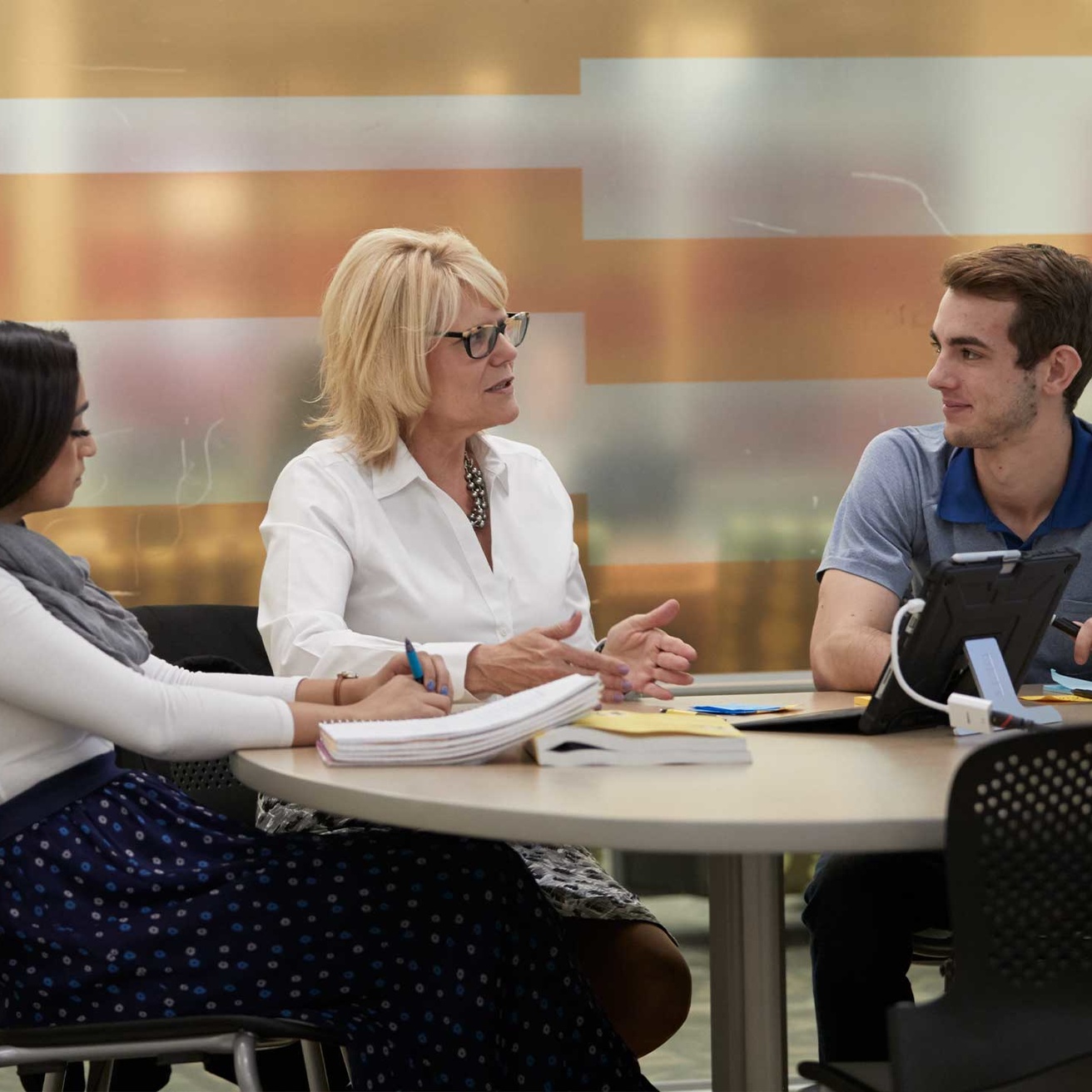 Woman professor sitting at table talking with two students
