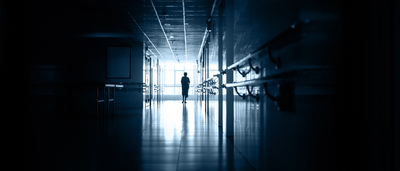 A photo illustration of a hospital corridor with a healthcare worker at the end.