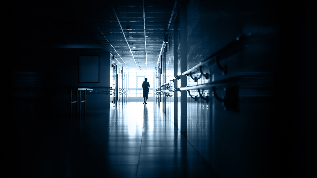 A photo illustration of a hospital corridor with a healthcare worker at the end.