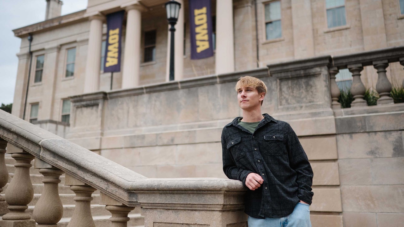 Tyler Kuecker standing on a step at the Old Capital leaning on a pillar looking off to the left